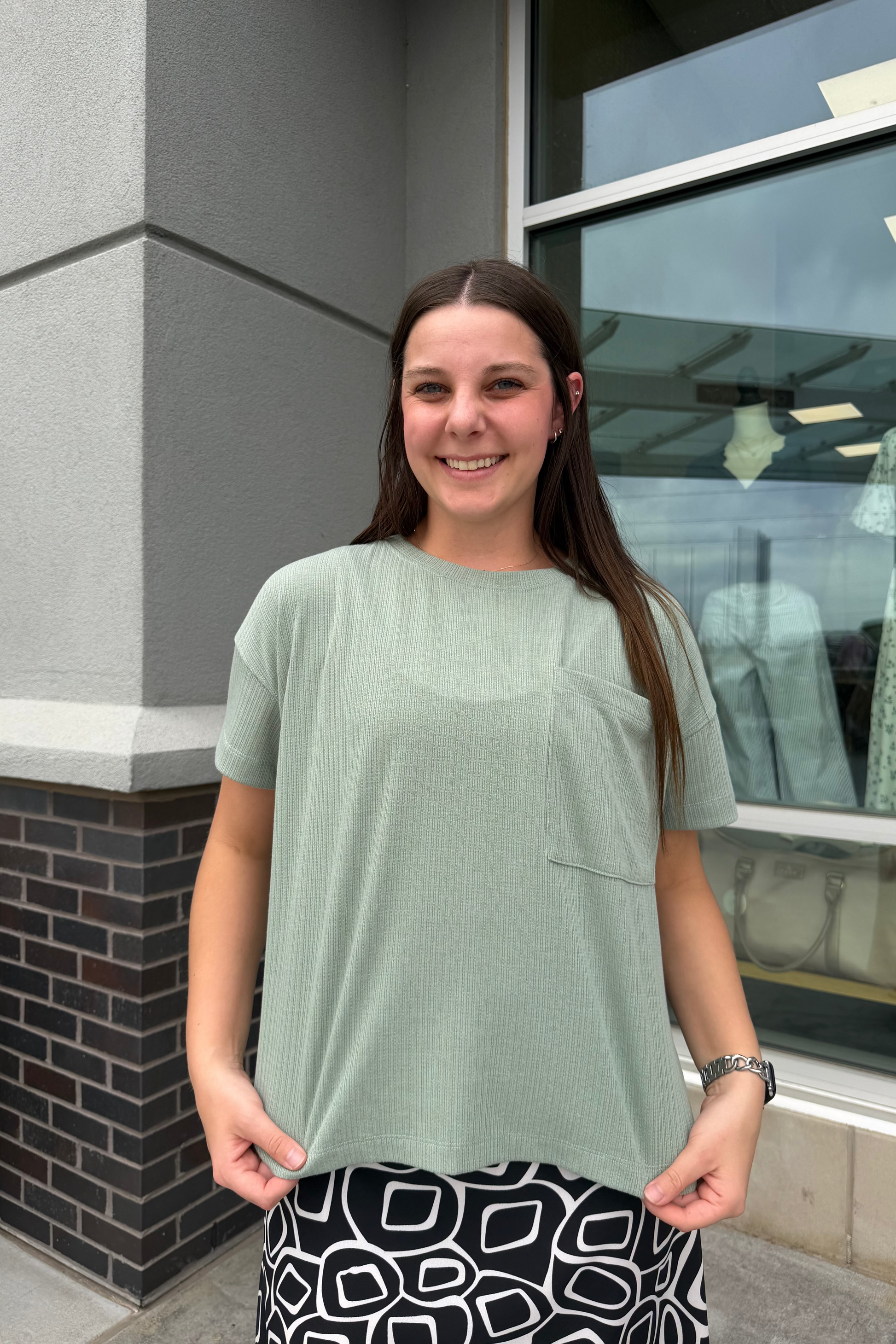Woman standing outside a building wearing a light green shirt and black and white patterned pants.