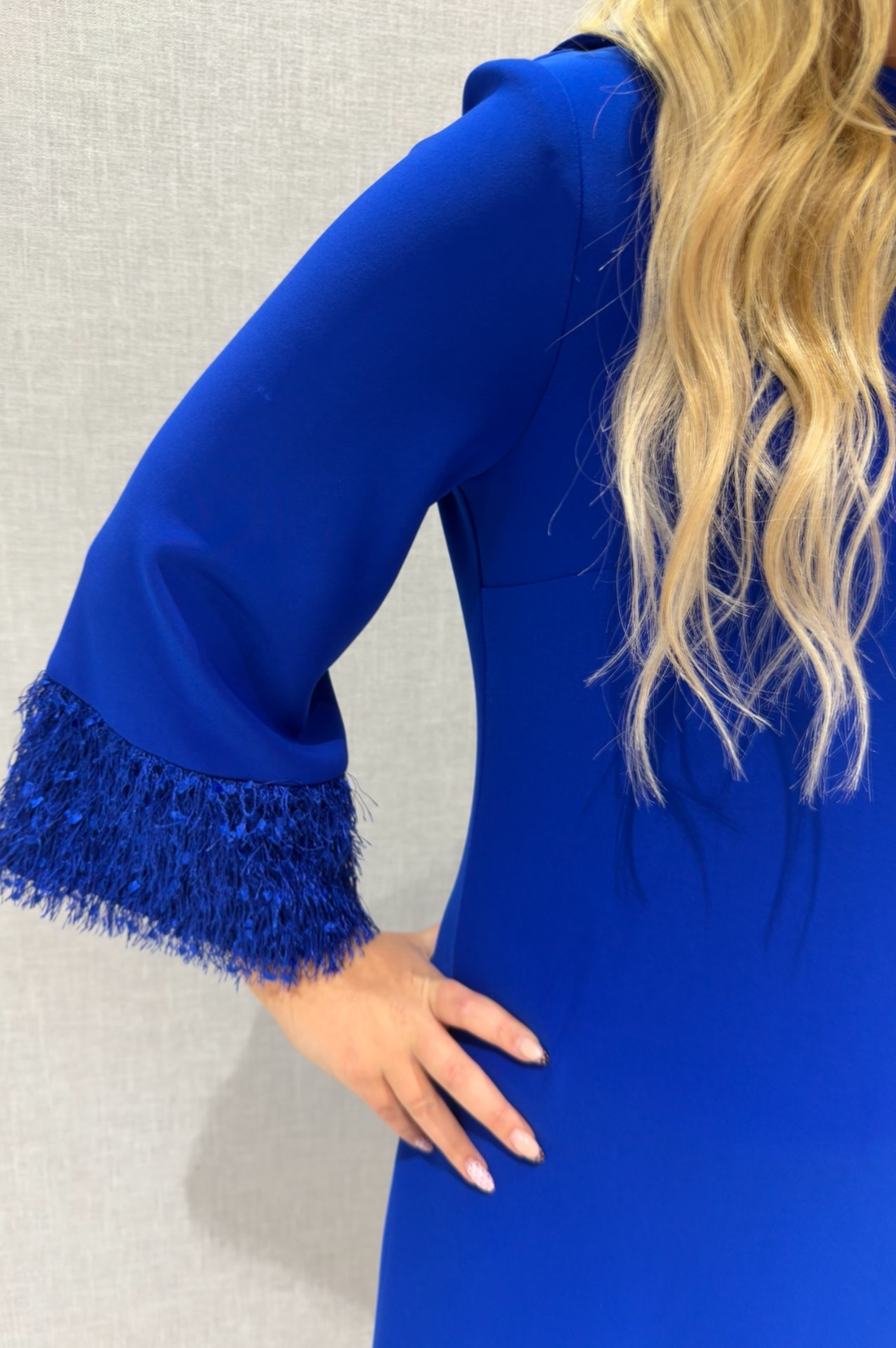 Blue dress with fringed cuffs worn by a person against a neutral background