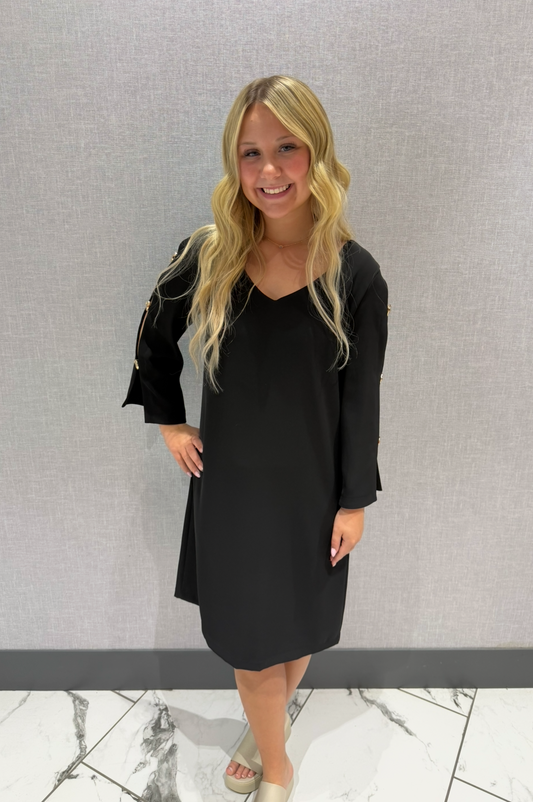 Woman wearing a black dress standing against a gray wall.