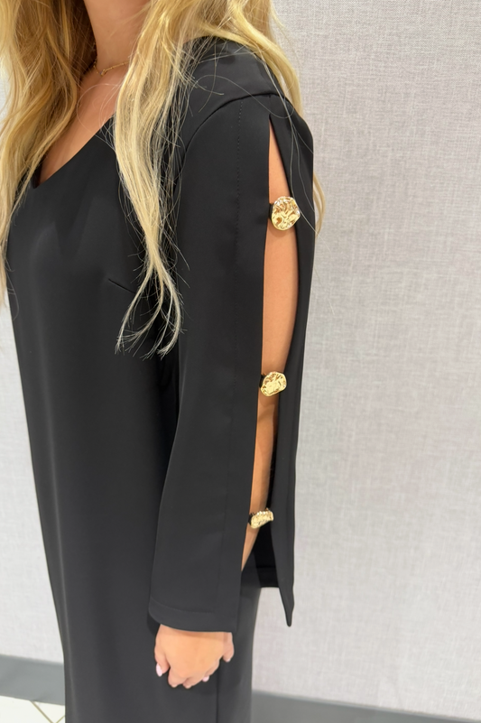 Black dress with gold accents worn by a person against a neutral background