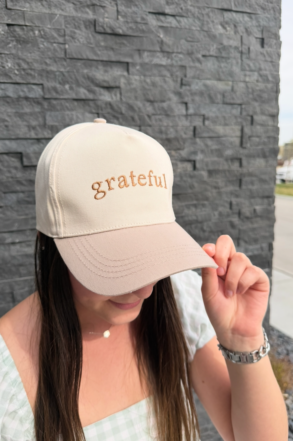 Person wearing a beige cap with 'grateful' text against a stone wall.