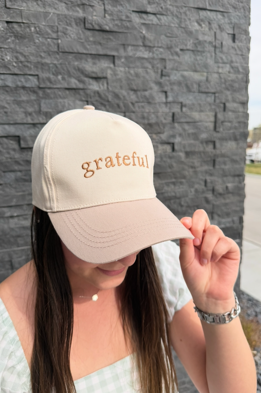 Person wearing a beige cap with 'grateful' text against a stone wall.