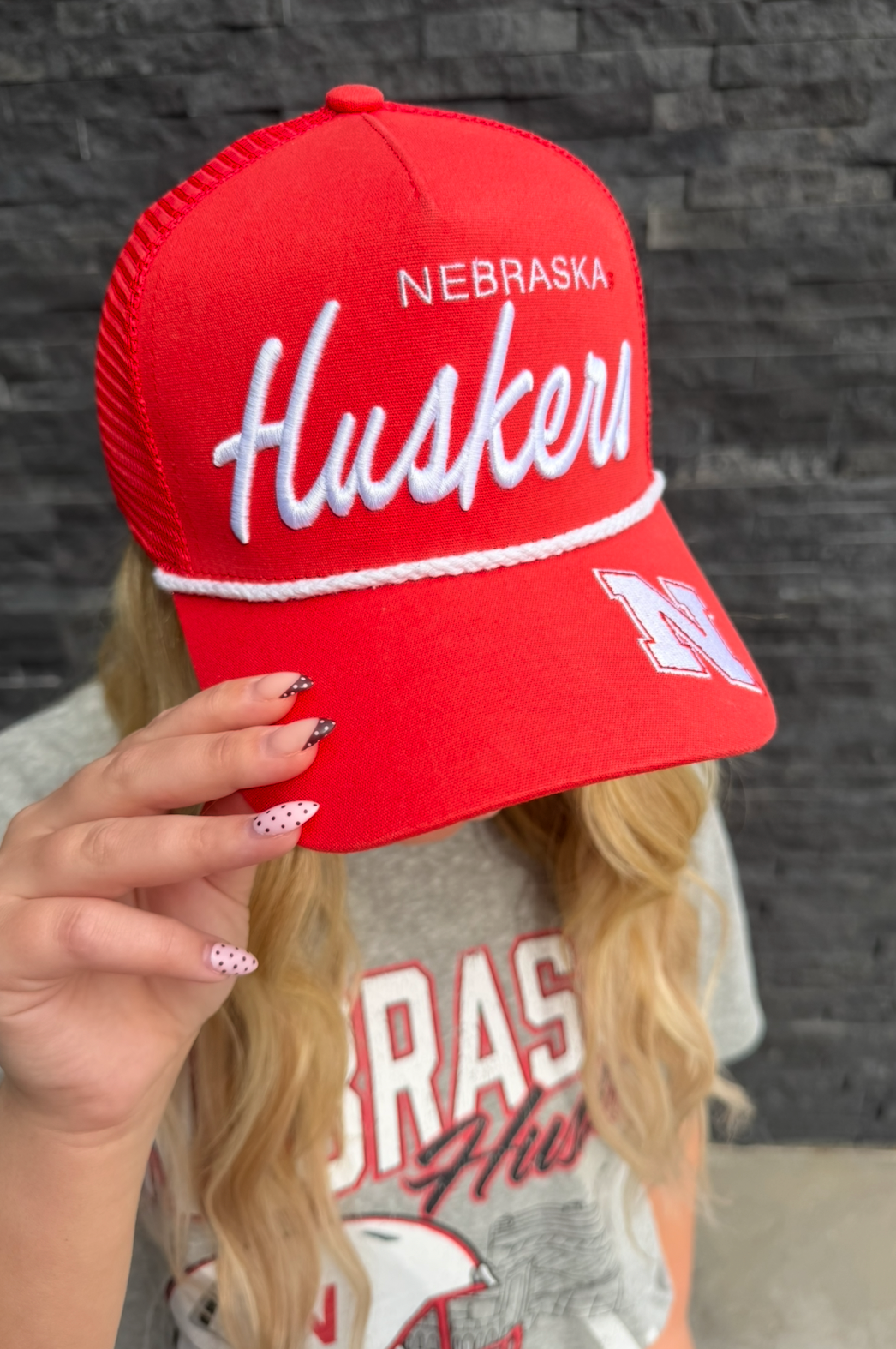 Red 'Nebraska Huskers' cap held by a person with a dark background