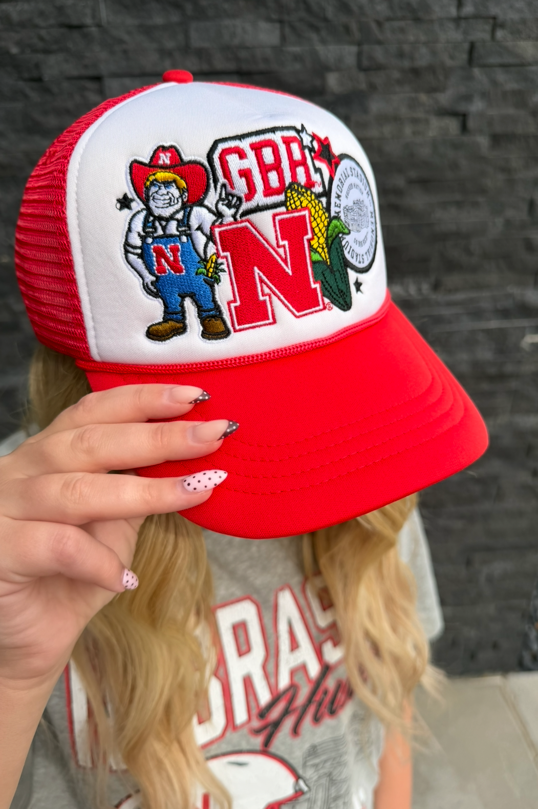 Red and white cap with a logo held by a person against a dark brick wall.