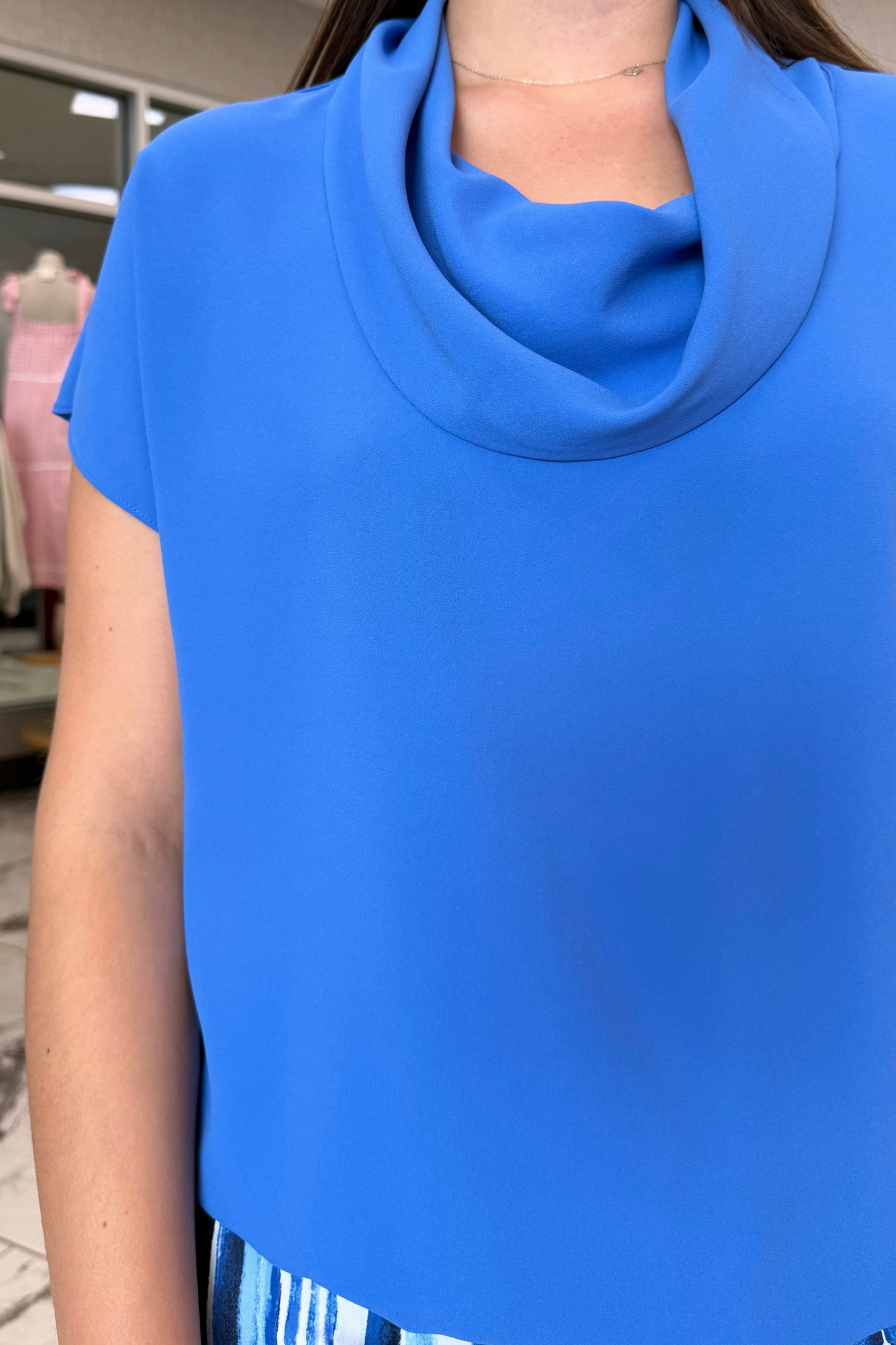 Person wearing a blue top with a cowl neck in a store setting