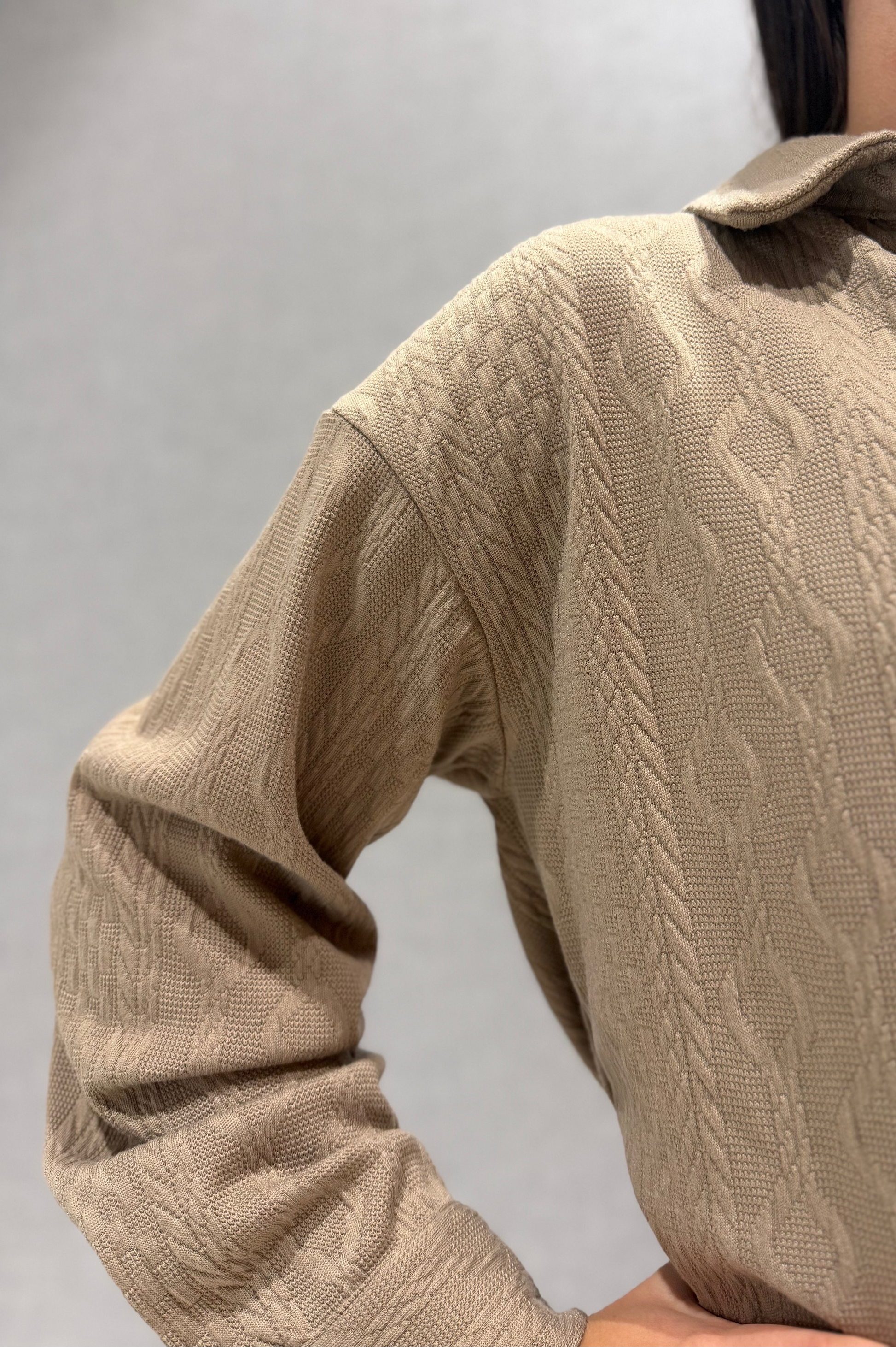Beige cable knit sweater worn by a person on a plain background
