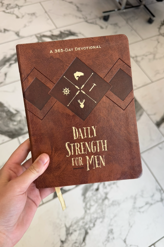 Brown notebook titled 'Daily Strength for Men' held by a hand on a marble surface.