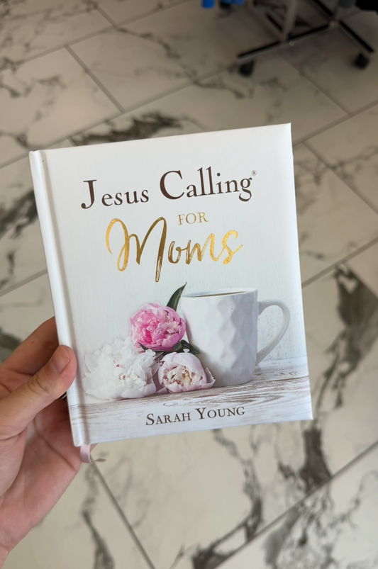 Book titled 'Jesus Calling for Moms' held by a person on a marble surface.