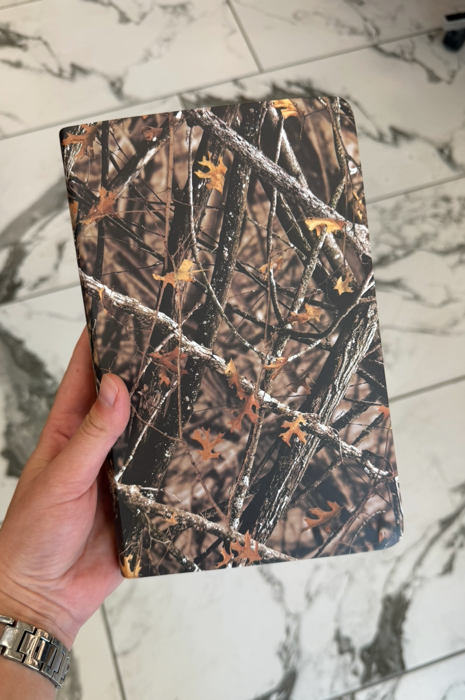 Camouflage-patterned notebook held by a hand on a marble surface