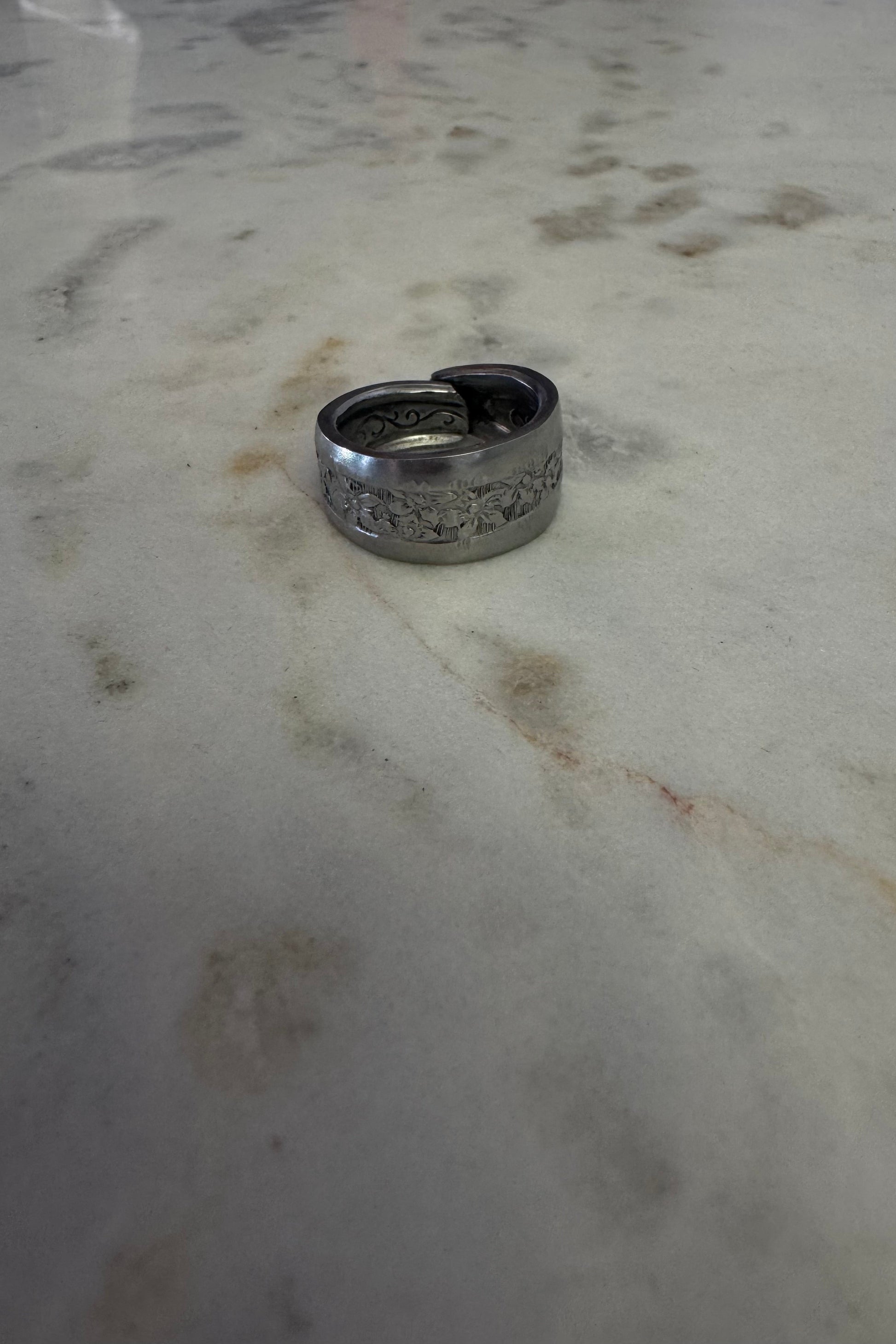 Silver ring with floral designs on a marbled surface