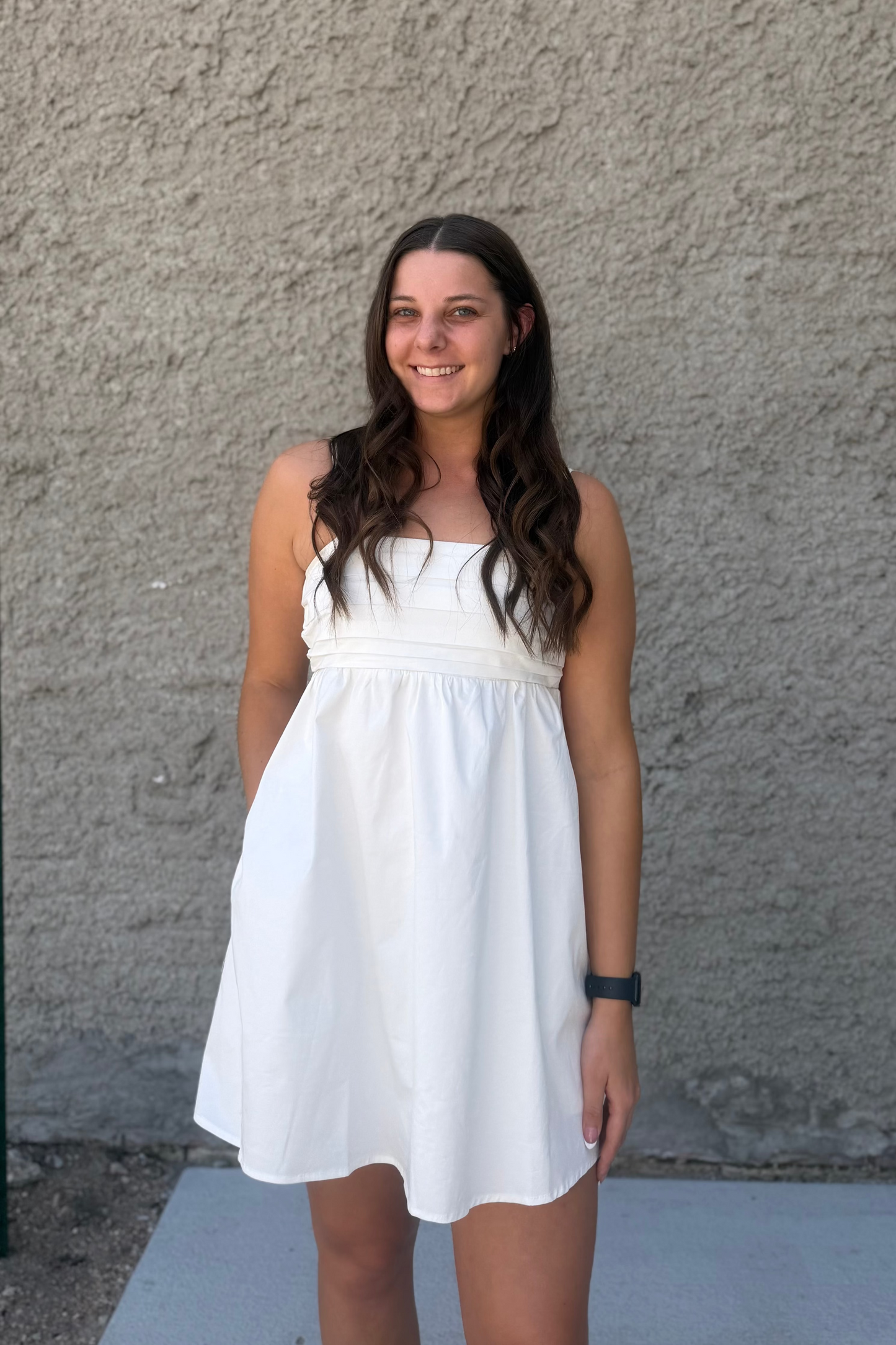 Woman in a white dress standing against a textured wall.