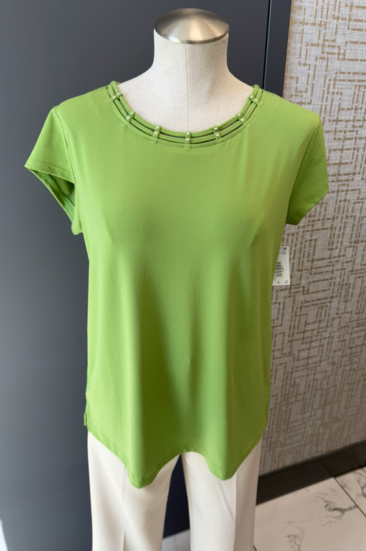 Green top on a mannequin against a gray wall.