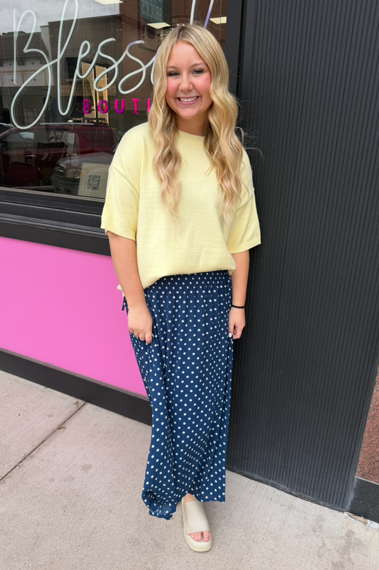 Person wearing a yellow top and blue polka dot pants standing in front of a store with a pink and black exterior.