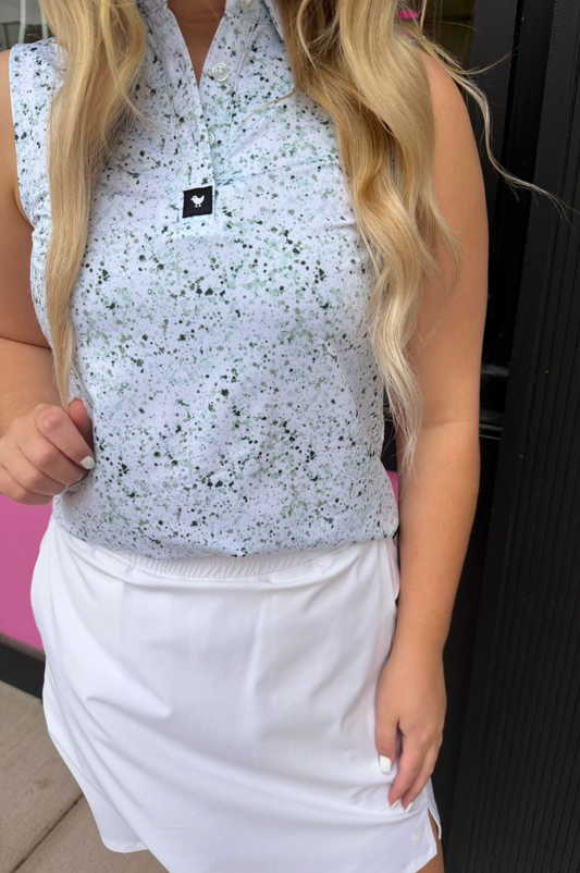 Person wearing a sleeveless patterned top and white shorts indoors.