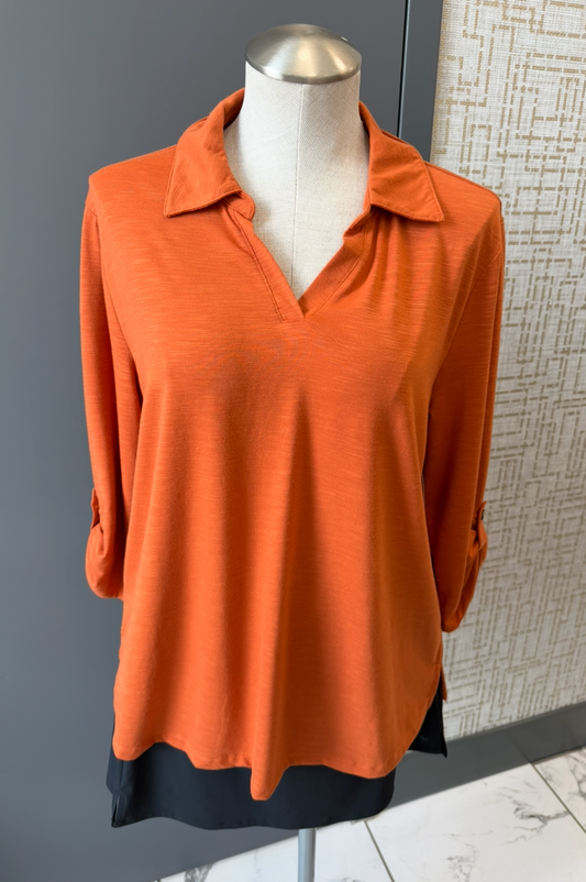 Orange long-sleeve top on a mannequin against a gray wall.