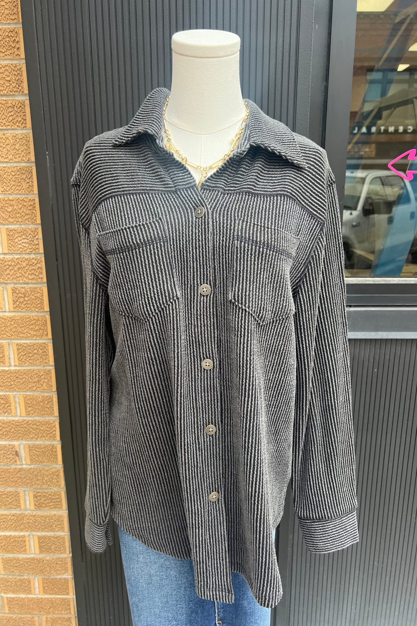 Gray striped shirt on a mannequin against a brick wall.