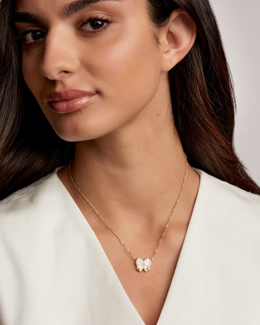 Close-up of a woman wearing a gold necklace with a butterfly pendant against a neutral background