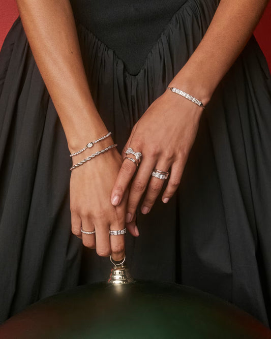 Close-up of hands wearing multiple rings and bracelets against a black background