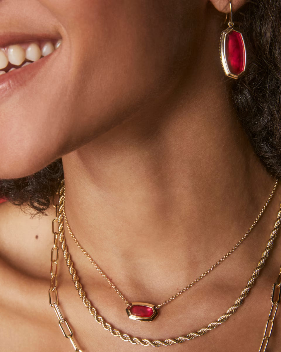 Close-up of a woman wearing gold necklaces and earrings with red gemstones.