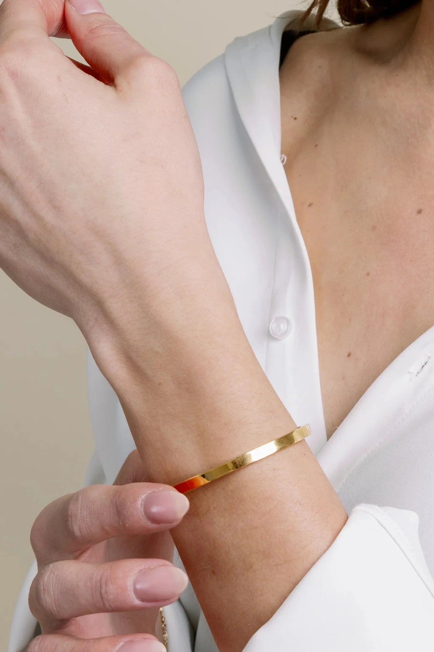 Person wearing a gold bracelet on a plain background