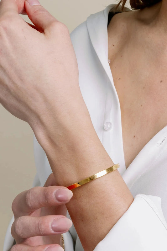 Person wearing a gold bracelet on a plain background