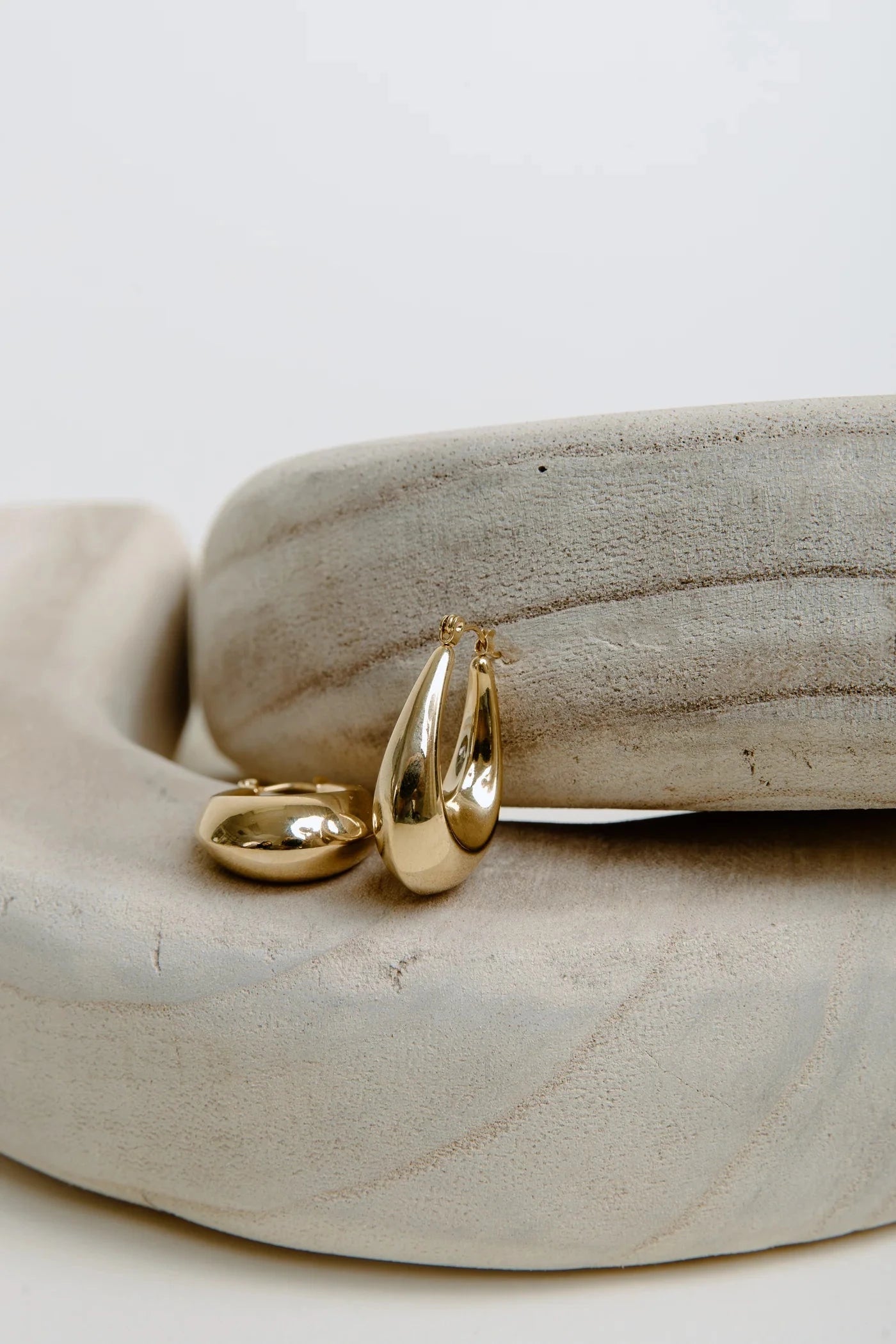 Gold teardrop-shaped earrings on a stone surface