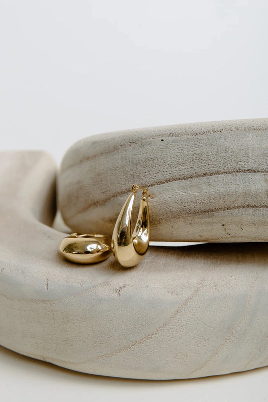 Gold teardrop-shaped earrings on a stone surface
