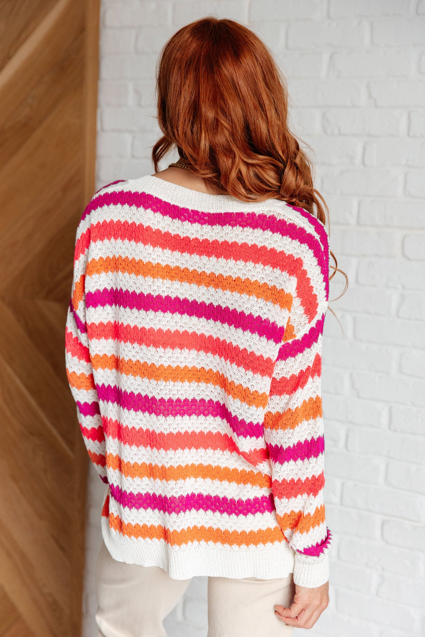 Person wearing a colorful striped sweater against a white brick wall.