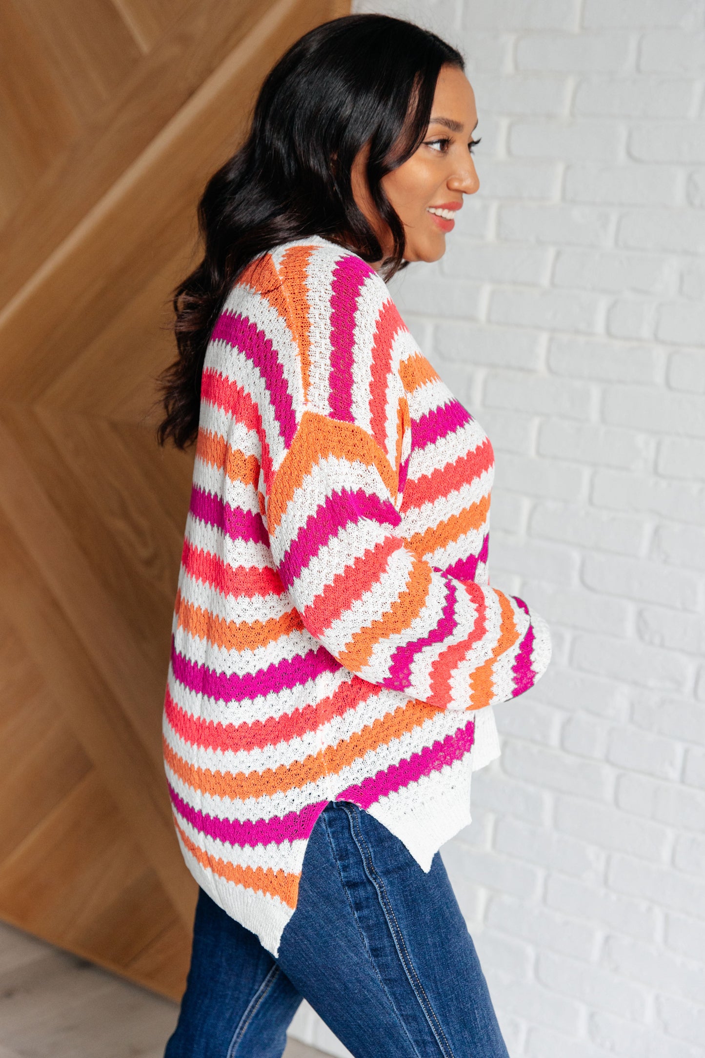Woman wearing a colorful striped sweater against a white brick wall.