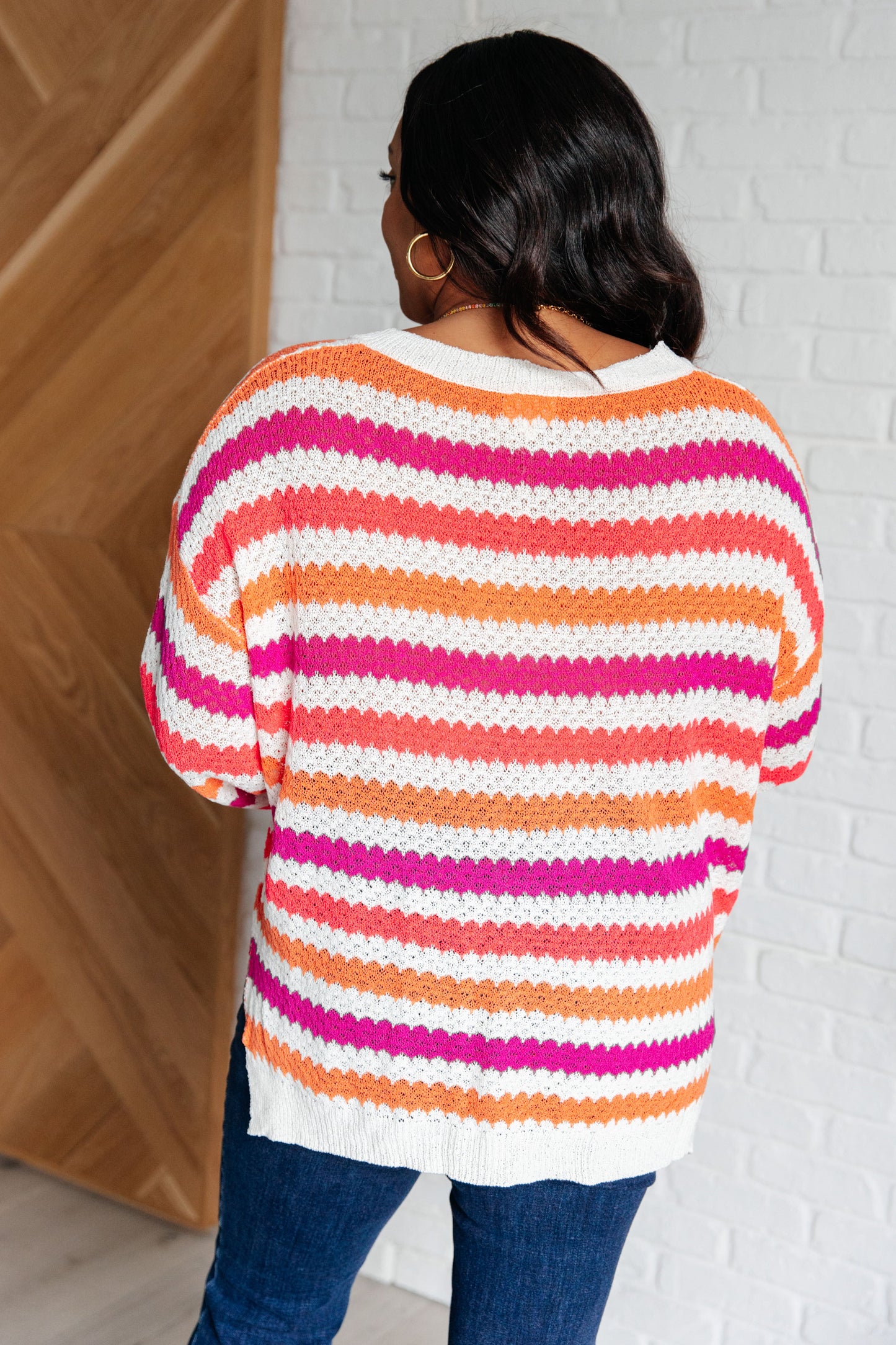 Person wearing a colorful striped sweater against a white brick wall.