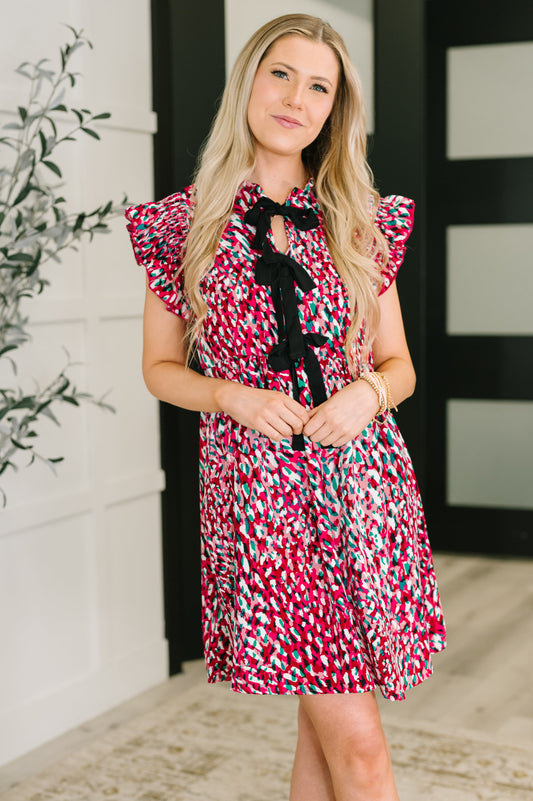 Woman wearing a colorful dress with a black bow tie in an indoor setting.