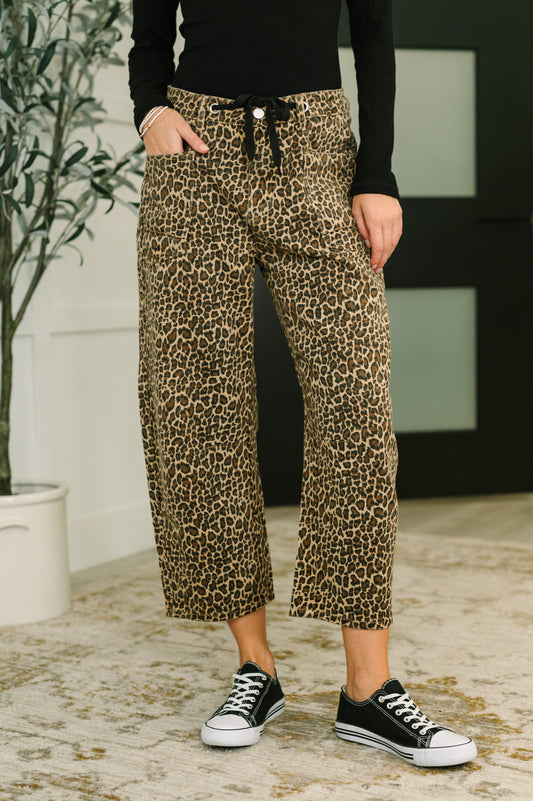 Person wearing leopard print pants and black sneakers indoors.
