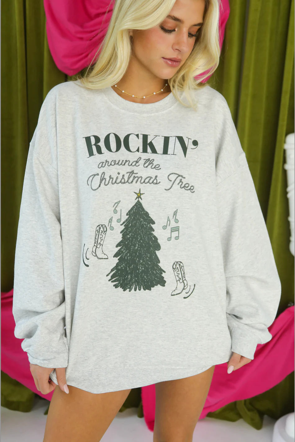 Woman wearing a gray sweatshirt with Christmas-themed design against a green curtain background