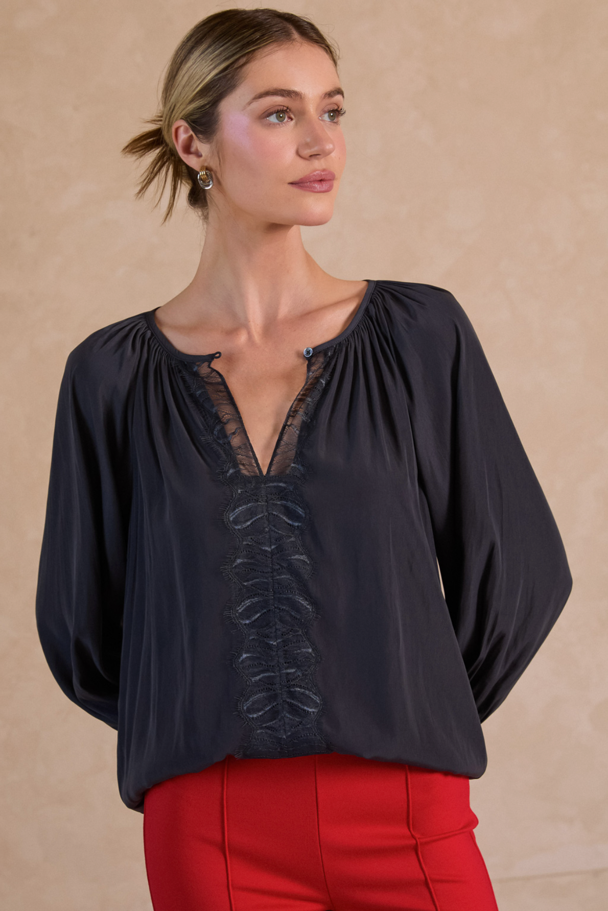 Woman wearing a black blouse with lace details and red pants against a beige background