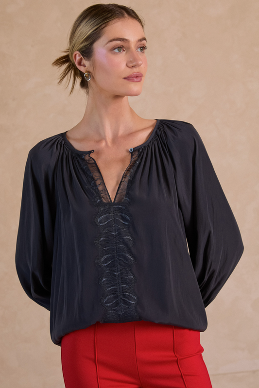 Woman wearing a black blouse with lace details and red pants against a beige background