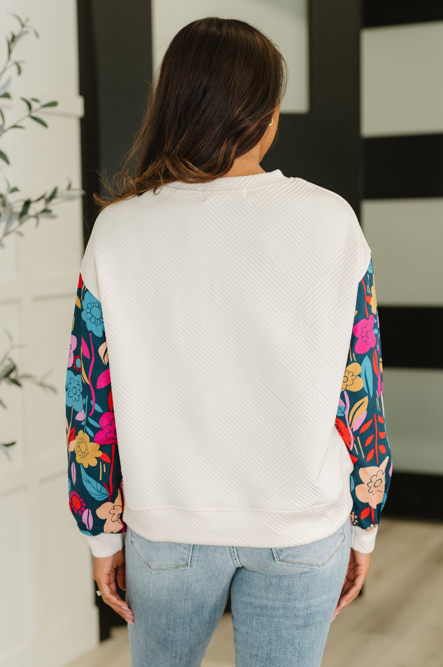 Person wearing a white sweatshirt with colorful floral sleeves in an indoor setting.