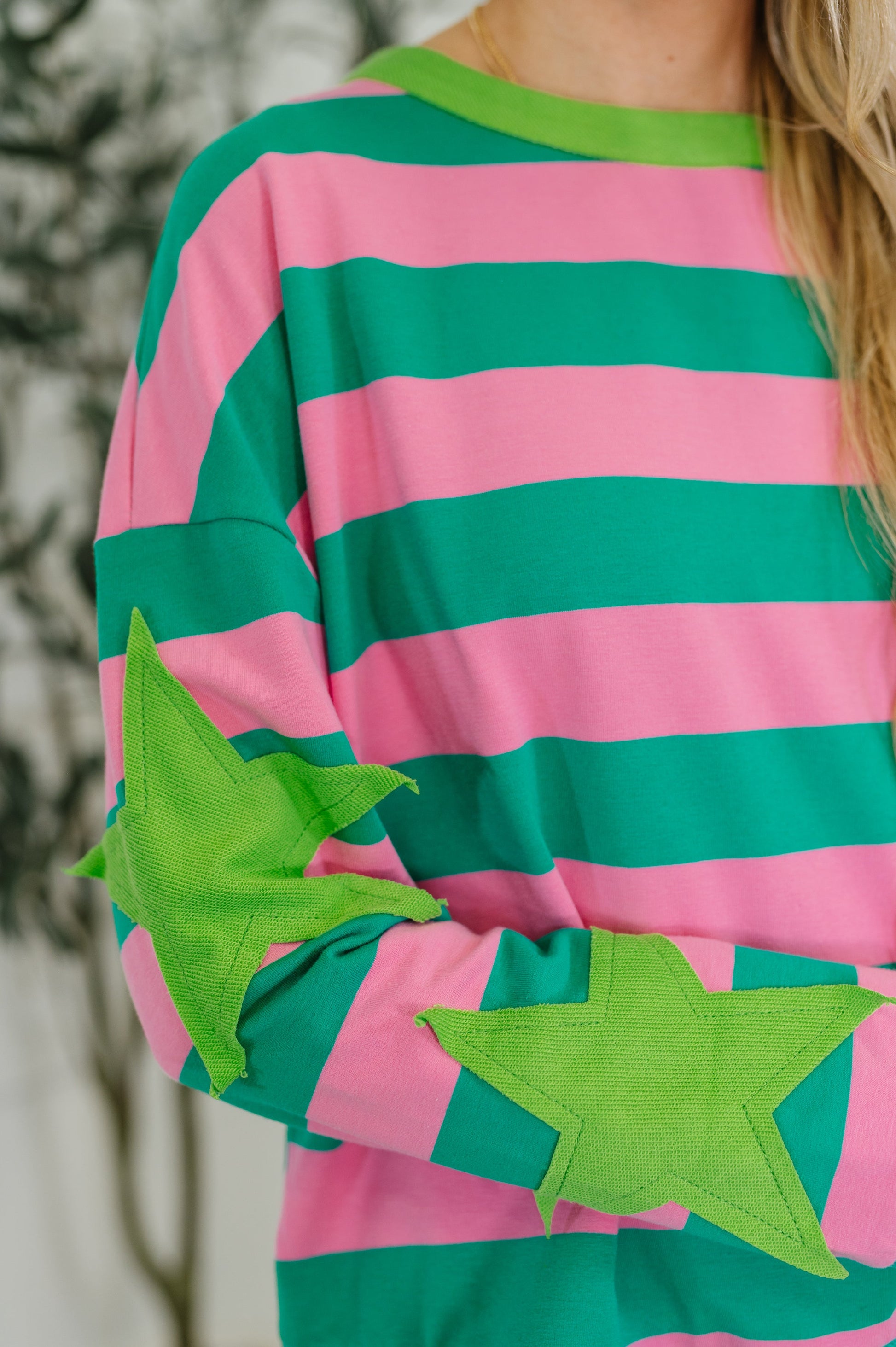 Person wearing a pink and green striped shirt with star designs on sleeves.