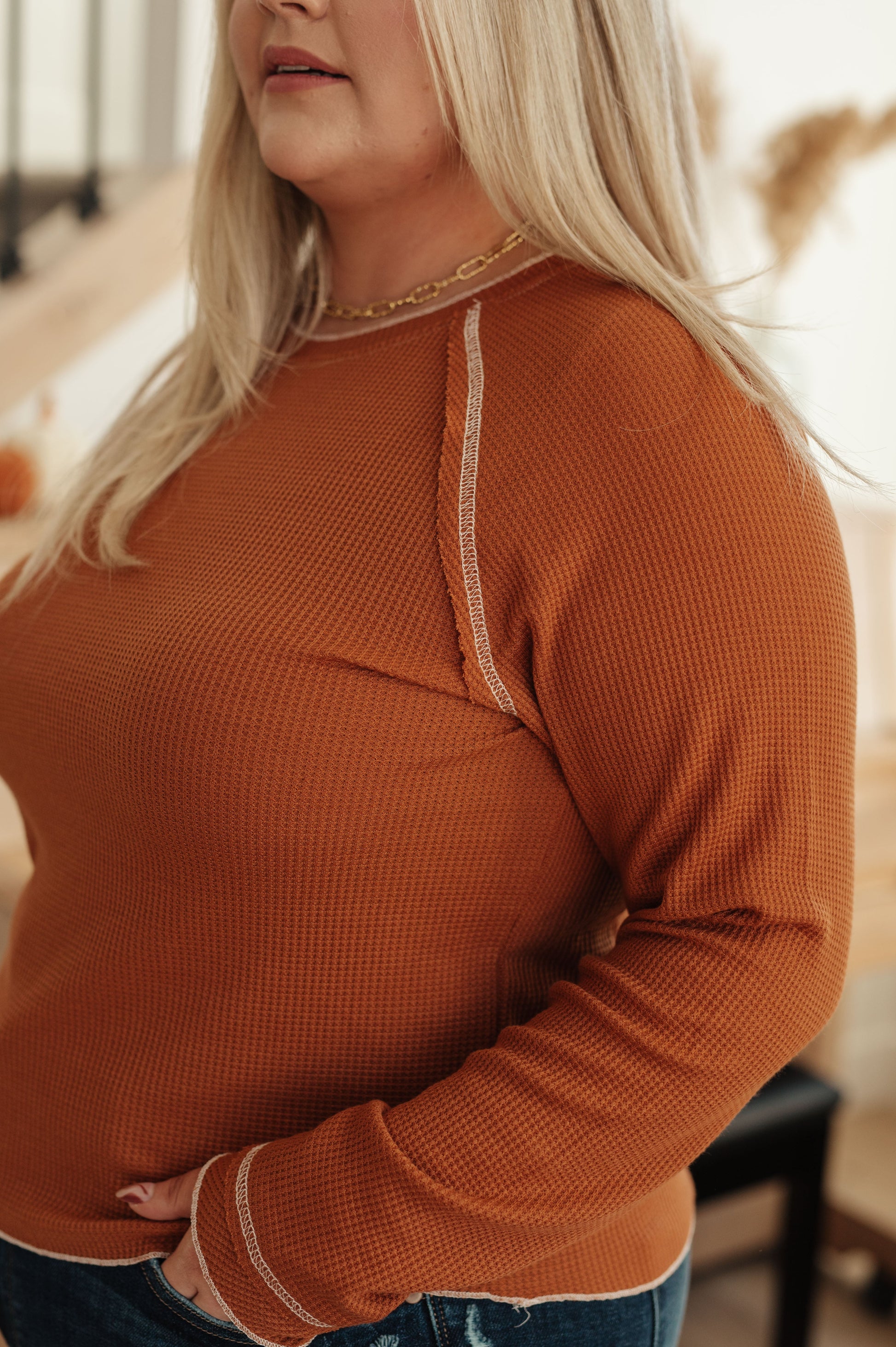 Person wearing a rust-colored long-sleeve top with white trim in a blurred indoor setting