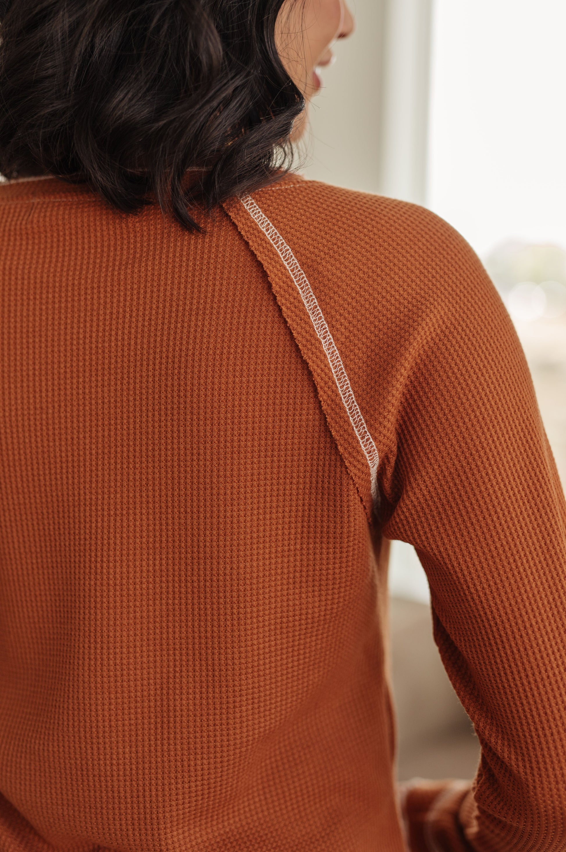 Person wearing a rust-colored textured sweater with thin straps.