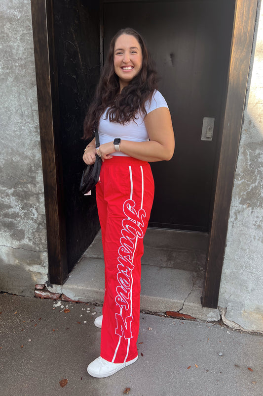 Woman wearing red pants with white text, standing outside a building.
