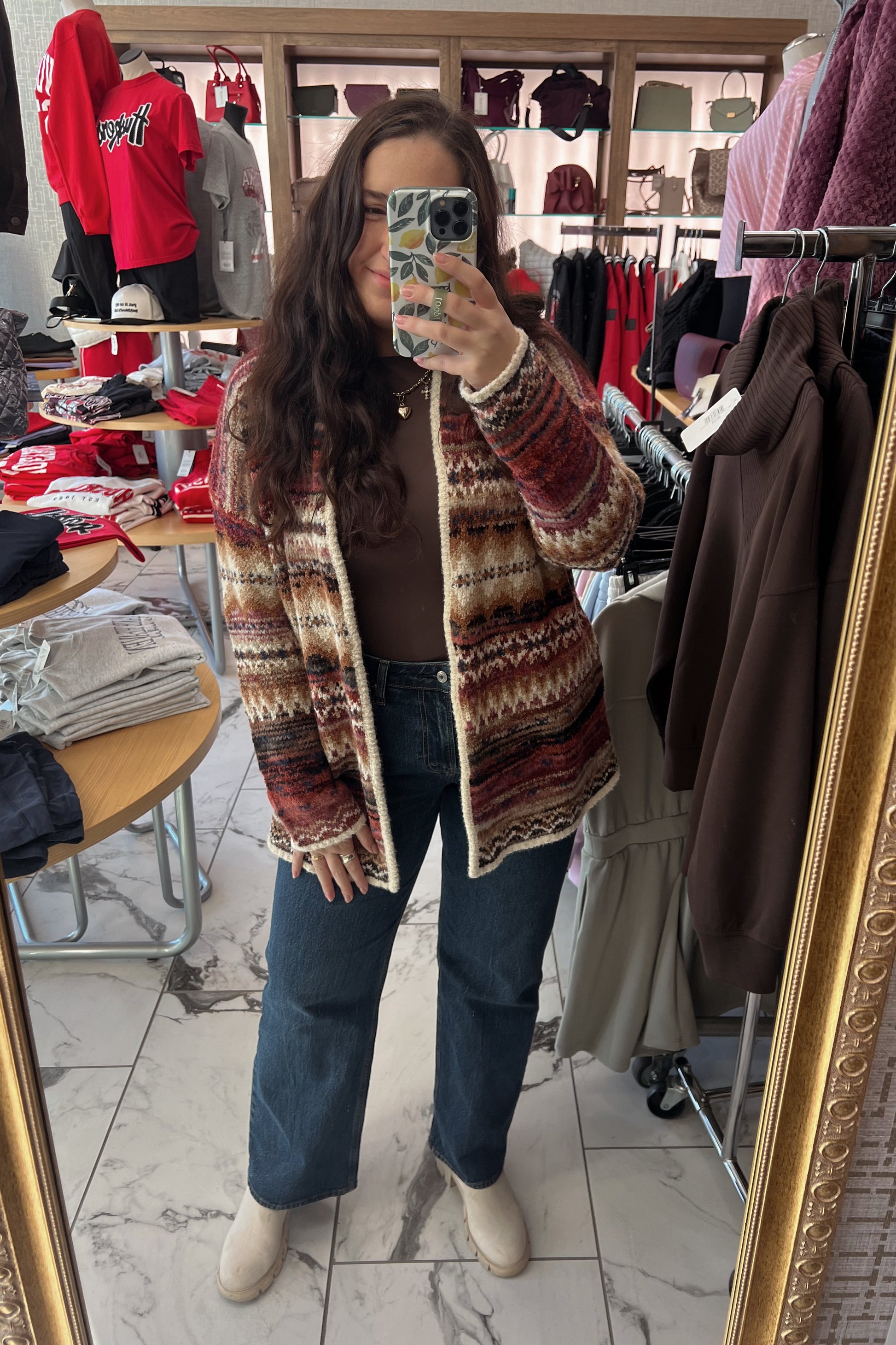 Person taking a mirror selfie wearing a patterned jacket in a clothing store.