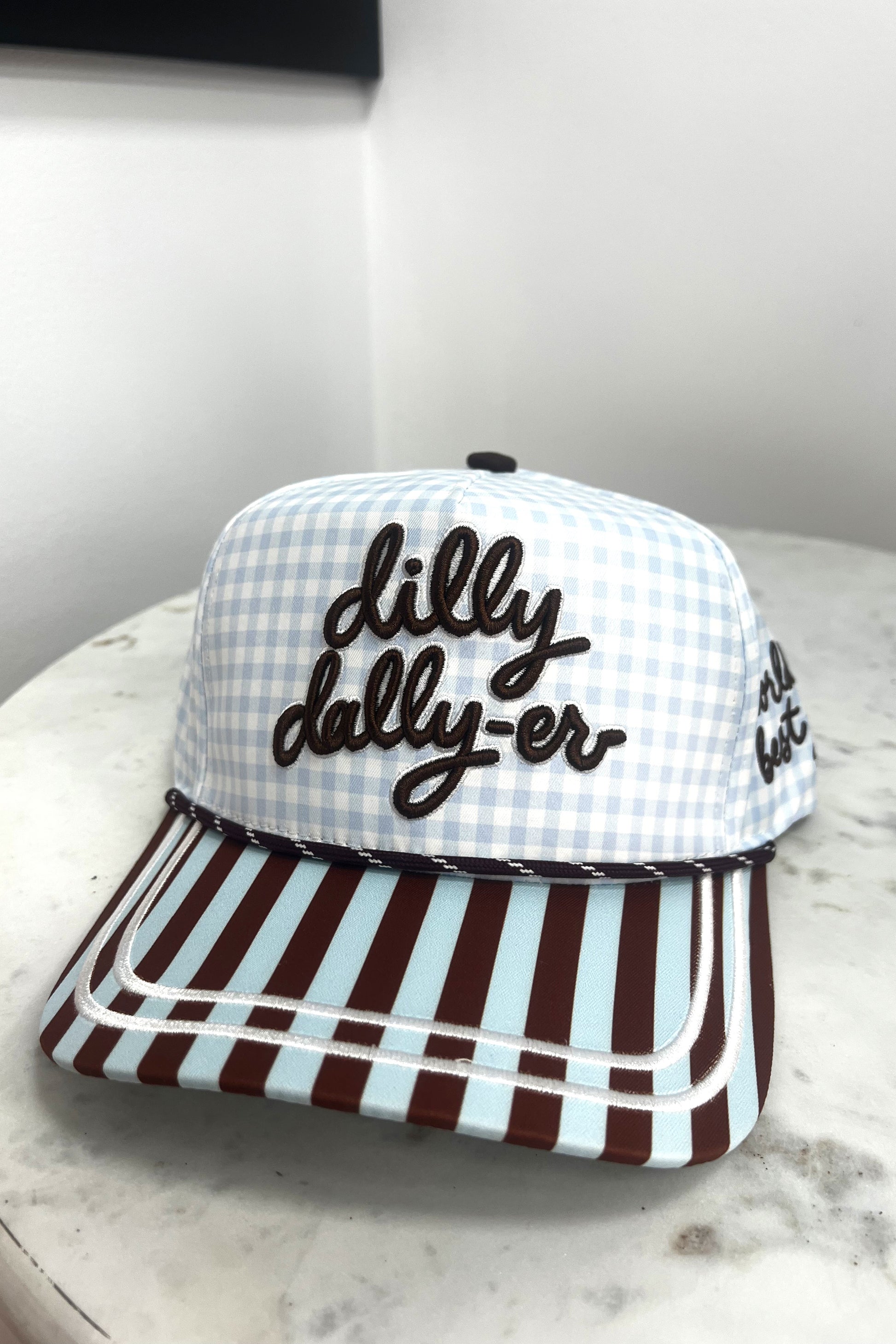 Checkered cap with 'dilly dally-er' text on a marble surface