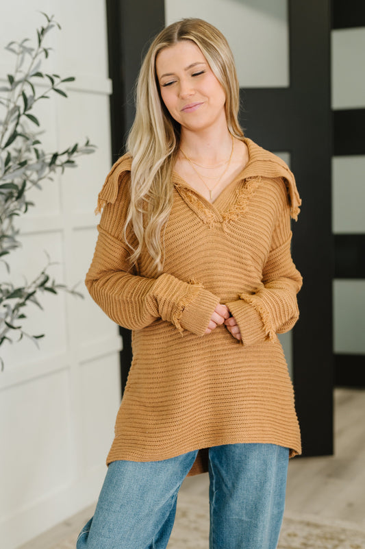 Woman wearing a brown ribbed sweater and blue jeans indoors.