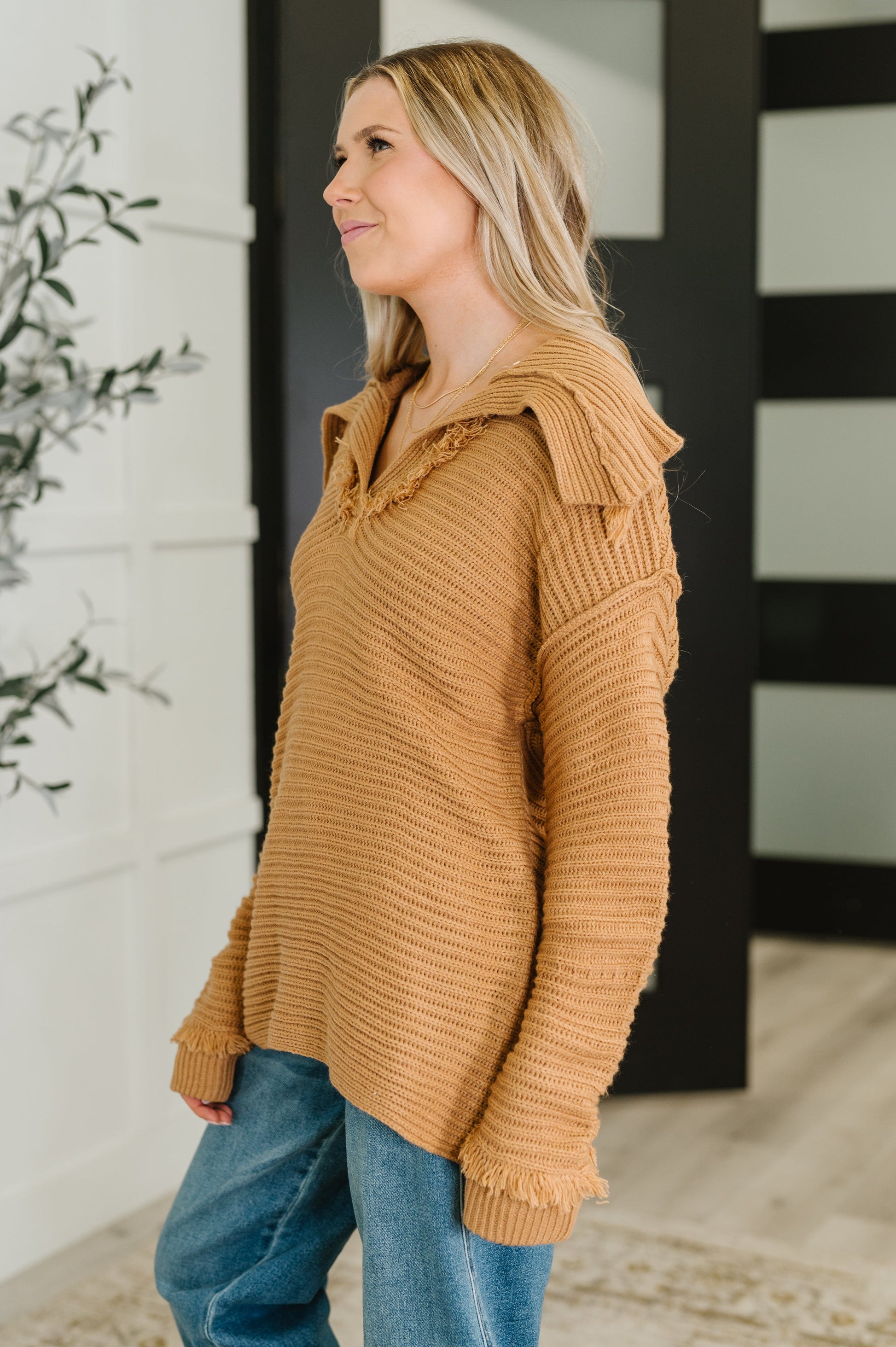 Woman wearing a brown sweater and blue jeans indoors.