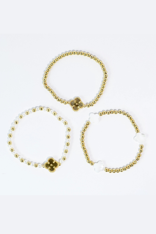 Three gold beaded bracelets with clover charms on a white background