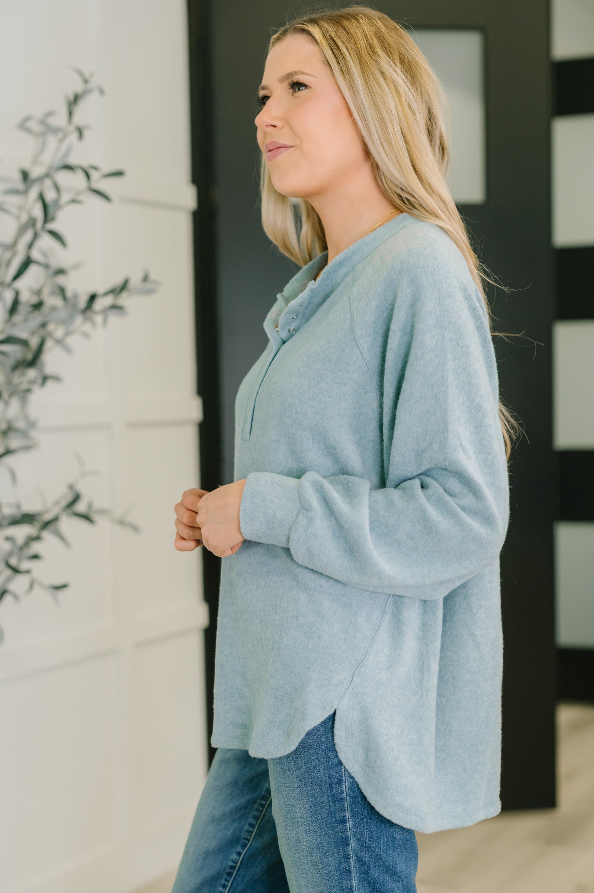 Woman wearing a light blue sweater and jeans standing indoors.