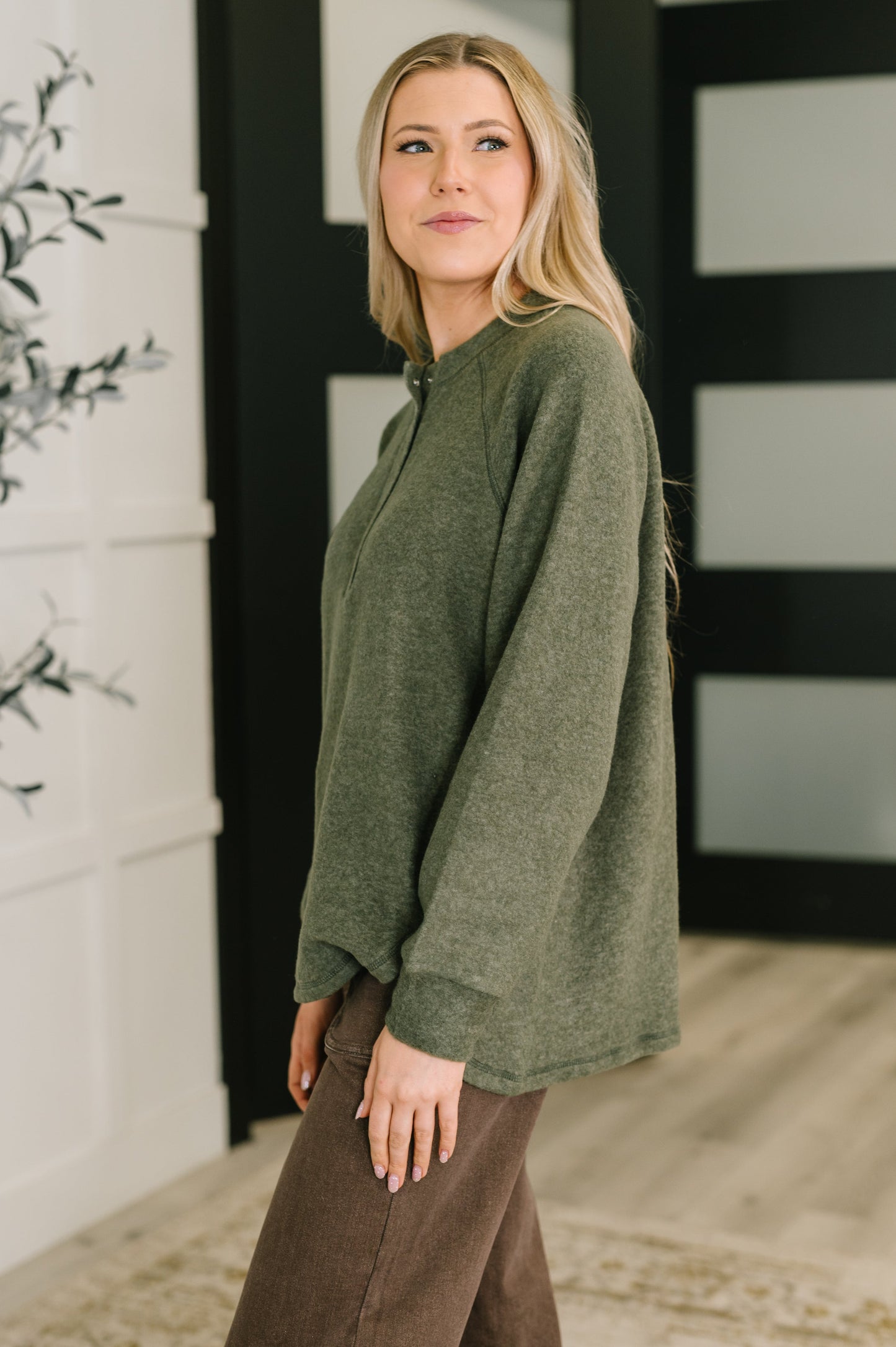 Woman wearing a green sweater and brown pants standing in a room with decorative elements.