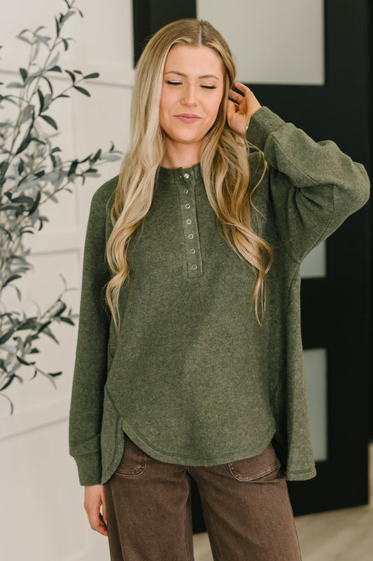 Woman wearing a green long-sleeve shirt and brown pants indoors.