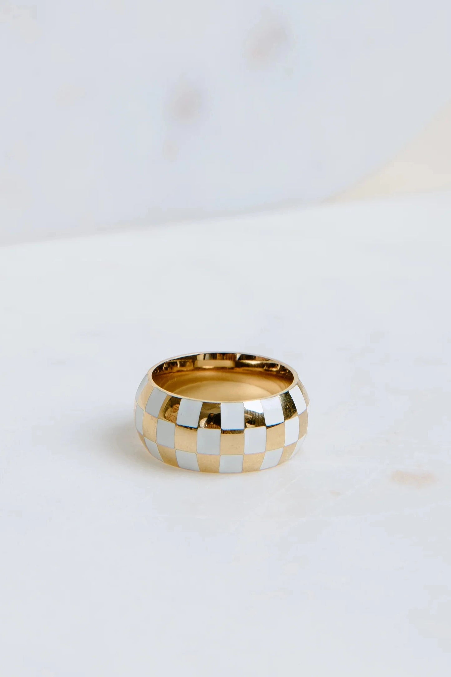 Gold and silver checkered ring on a white surface