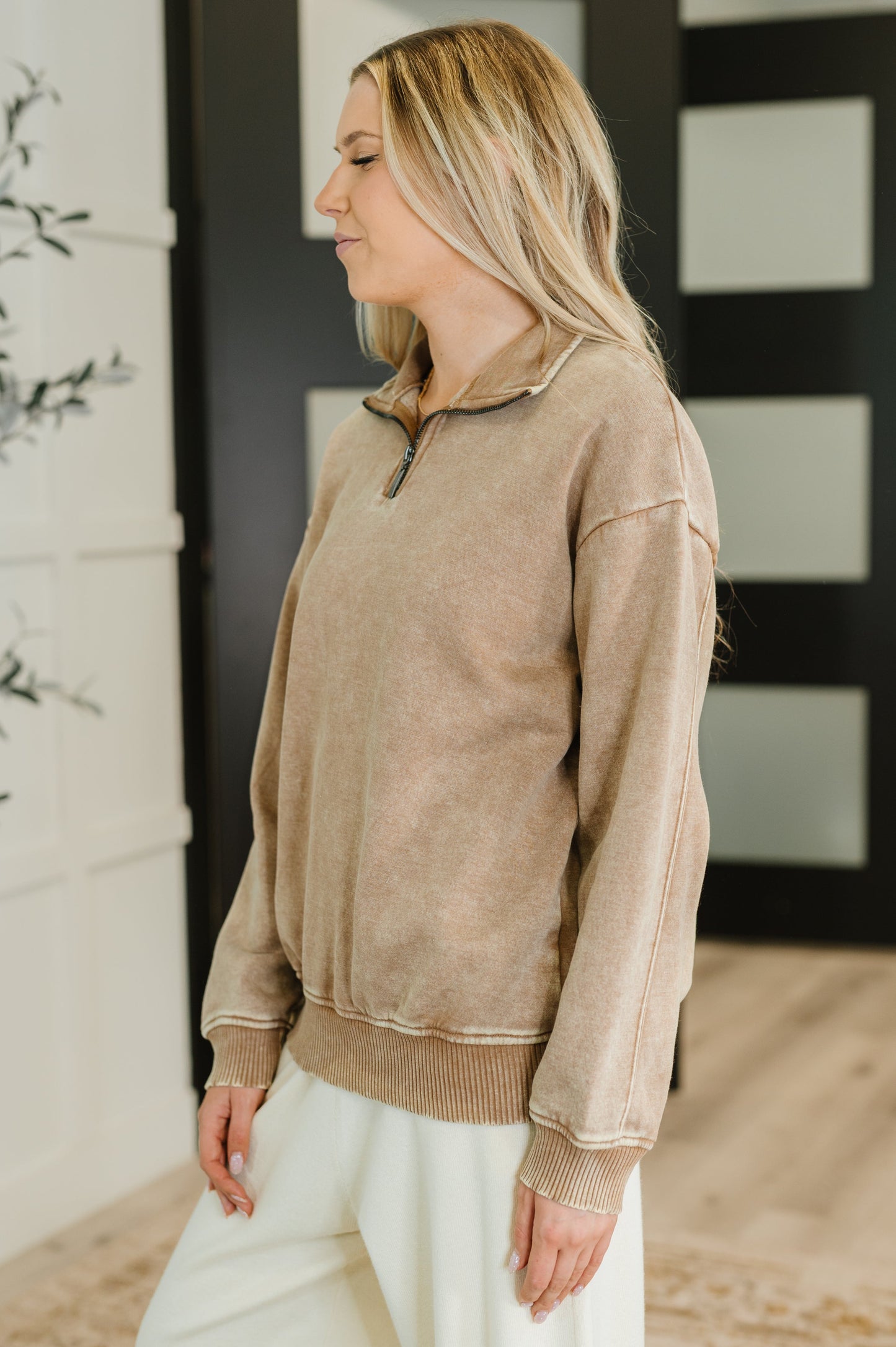 Woman wearing a beige jacket in a room with a decorative wall.